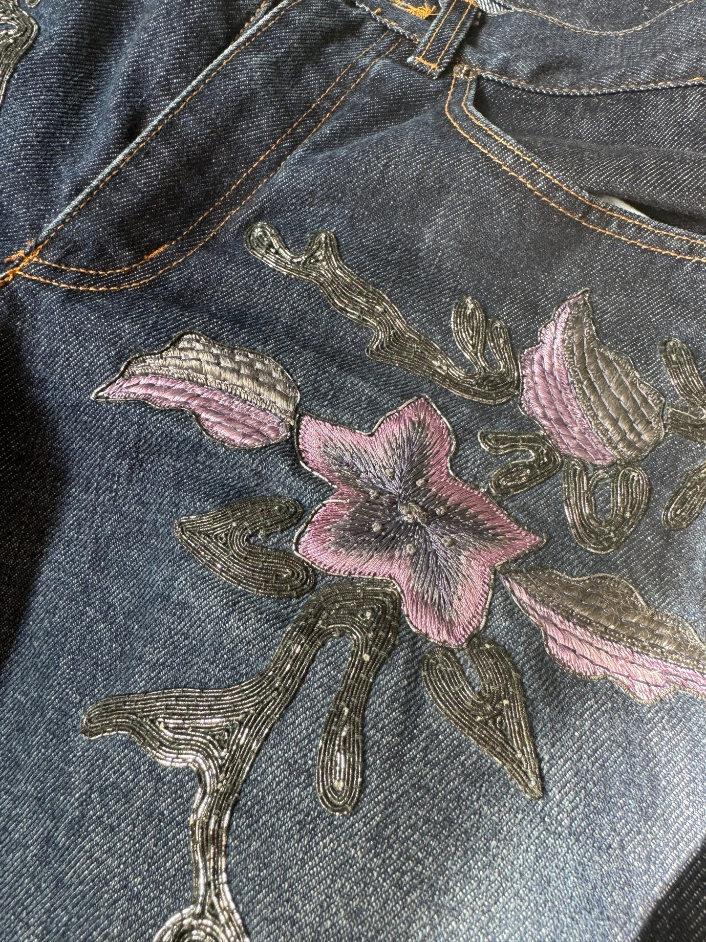 Denim jeans with metallic soutache embroidery and purple flowers.