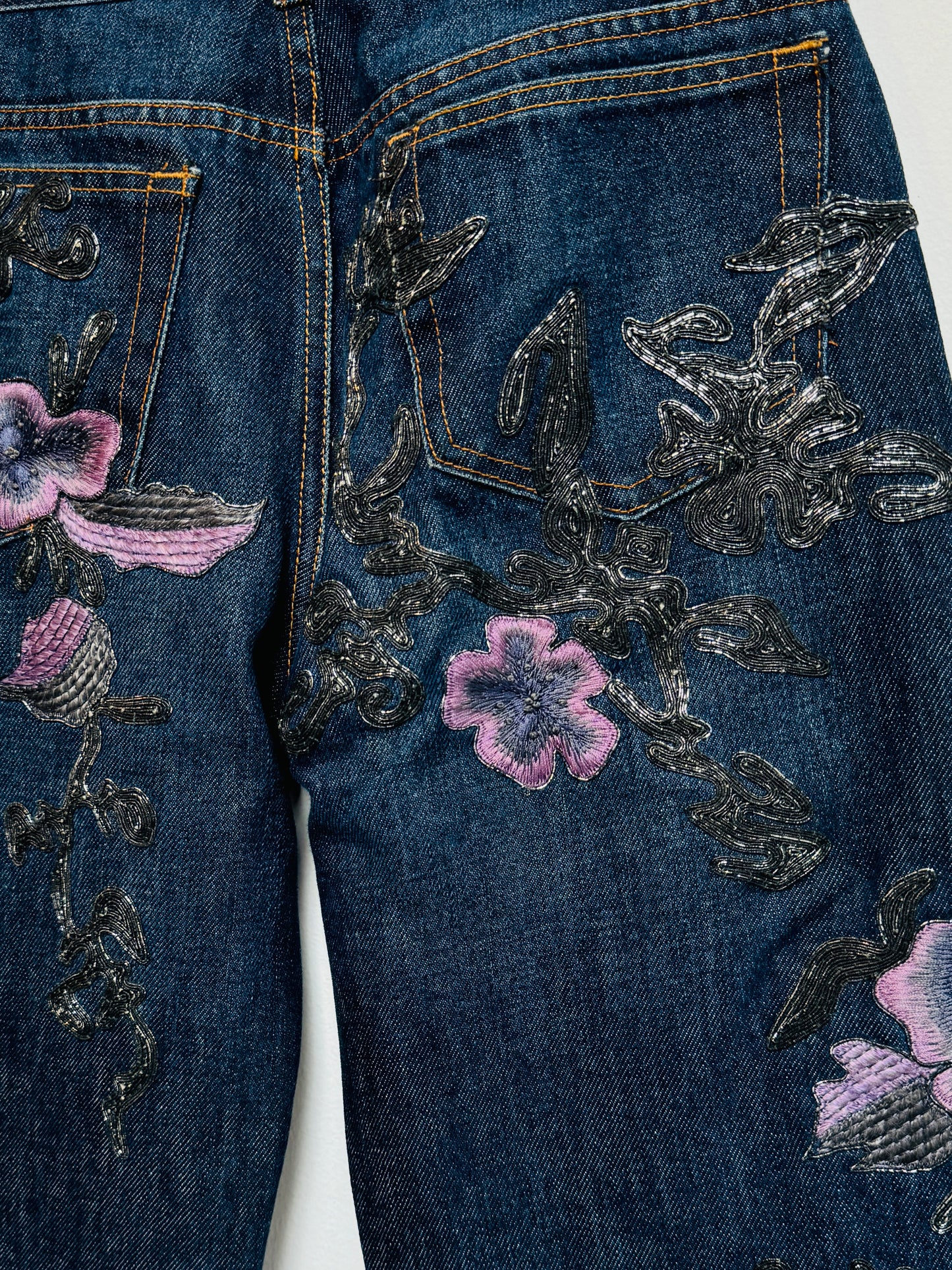 Denim jeans with metallic soutache embroidery and purple flowers.