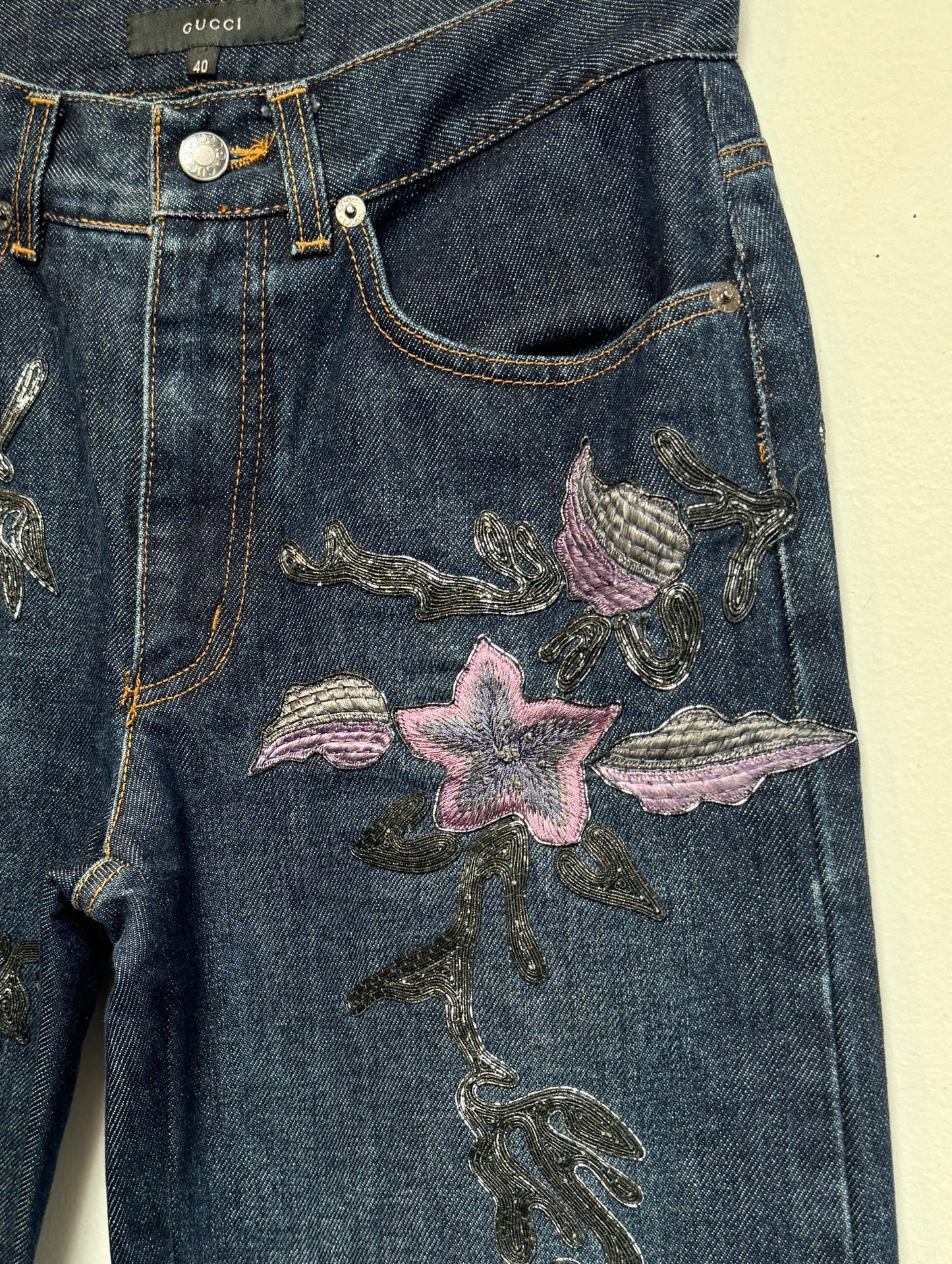 Denim jeans with metallic soutache embroidery and purple flowers.
